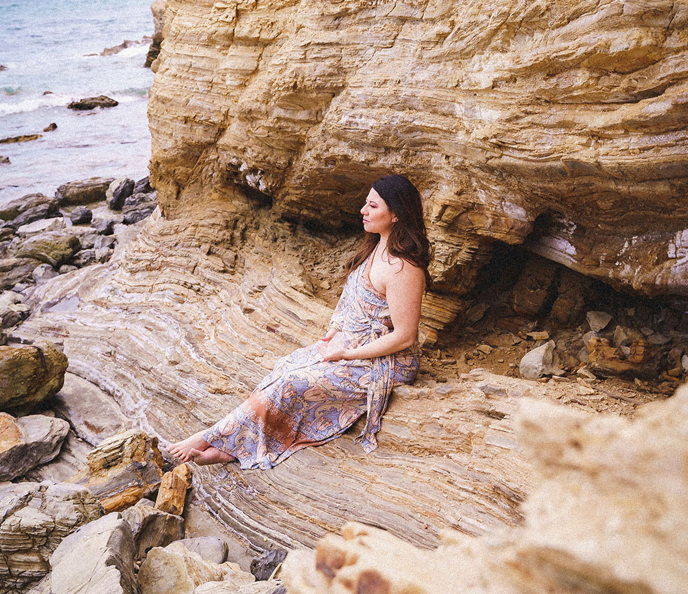 Desiree de Lunae sitting on a rocky shoreline